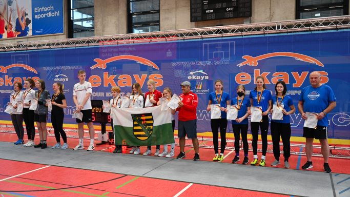 Gruppenfoto von Teilnehmern mit Medaillen bei einer Sportveranstaltung in einer Halle.